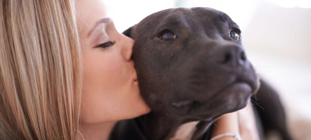 A young woman kisses a black dog